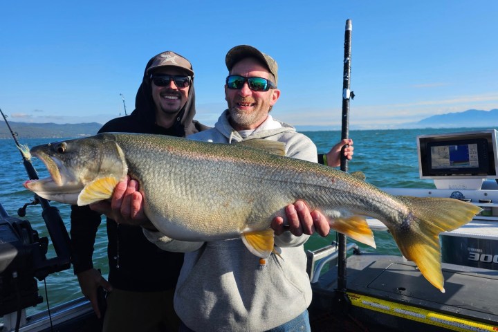 Two men on a boat holding a large fish with a fishing pole.