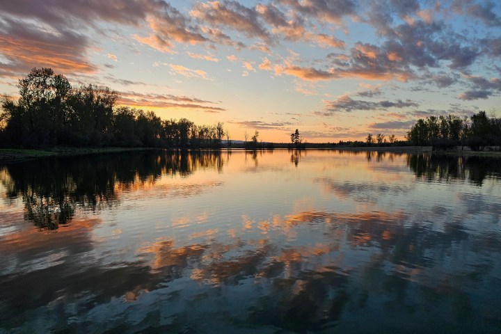 Sunset over a calm lake with reflections of colorful clouds and silhouetted trees.