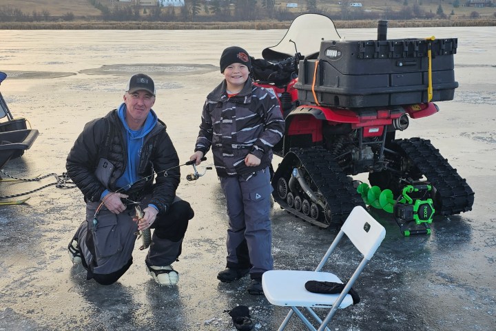 Two people ice fishing near an ATV on a frozen lake.