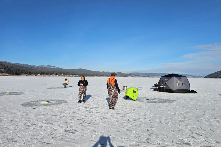 People ice fishing on a snowy lake with a tent and gear.