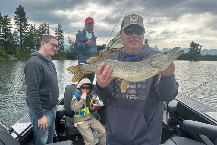 Group of four on a fishing boat, man in foreground holding a large fish.