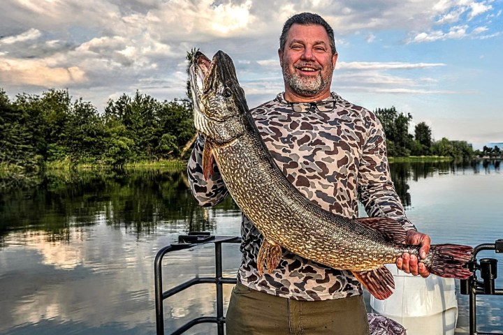Man holding a large fish on a boat in a lake.