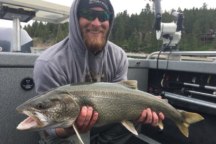 Person in hoodie holding a large fish on a boat.