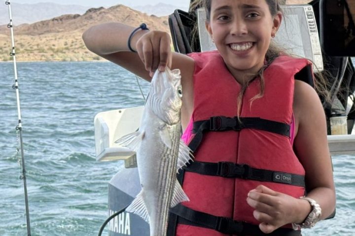 Girl in red life jacket holding a fish on a boat.