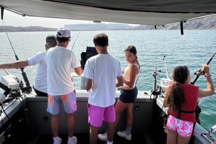 Four people fishing on a boat in a lake with mountains in the background.