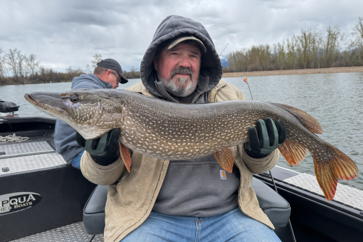 Man holding a large fish on a boat, cloudy sky background.