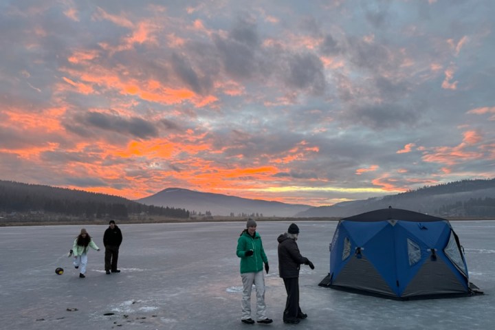 People on a frozen lake with a tent, under a colorful sunset sky.