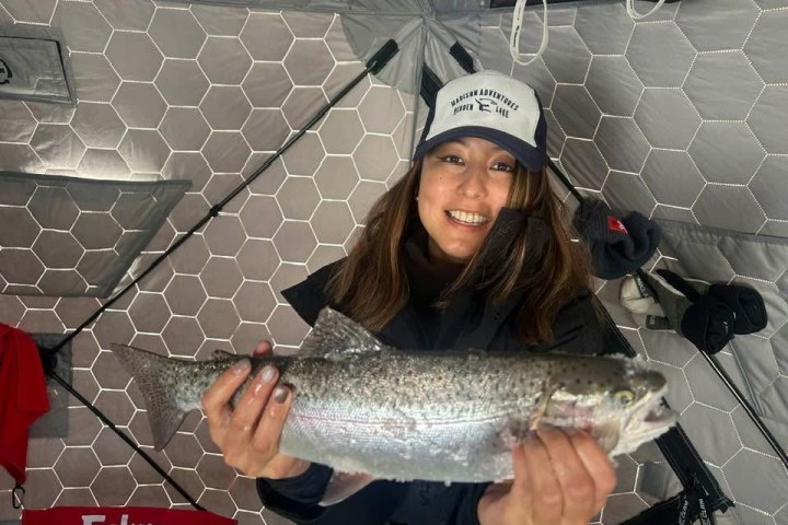 Person smiling, holding a fish inside a tent.