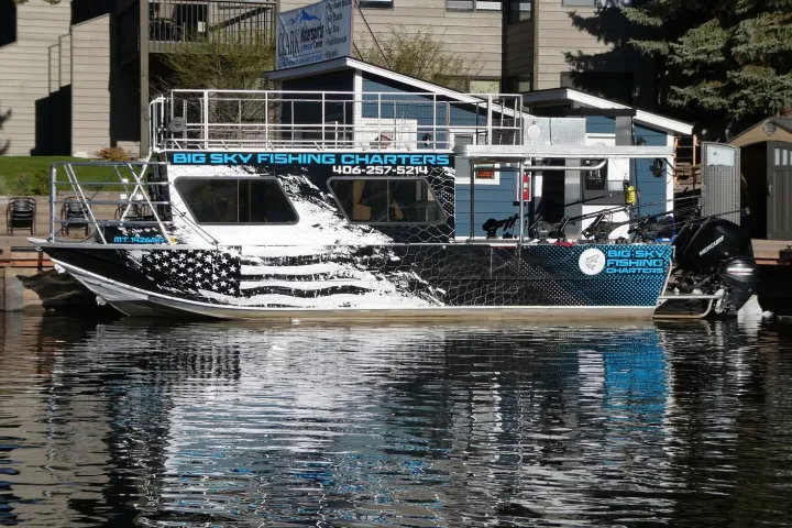 Fishing charter boat docked, with a black and white U.S. flag design and Big Sky Fishing Charters logo.