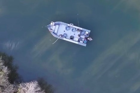 Aerial view of a solitary boat on calm water near a wooded shoreline.