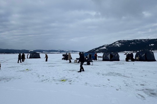 People ice fishing on a frozen lake with tents under cloudy skies.