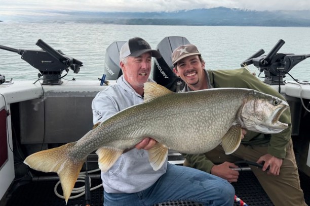 Two men on a boat holding a large fish, smiling at the camera.