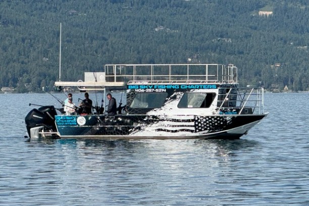 Boat on lake with people fishing, forested hills in background.
