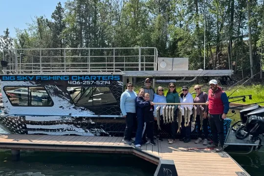Group of people holding fish in front of a boat on a dock.