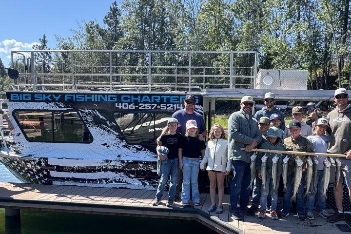 Group of people holding fish in front of a fishing charter boat on a sunny day.