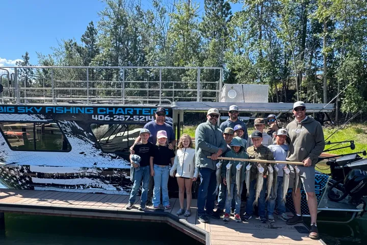 Group of people holding fish in front of a fishing charter boat on a sunny day.