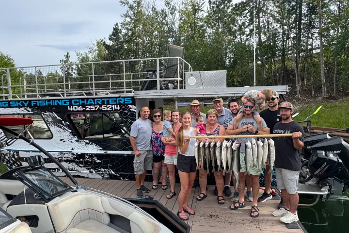 Group holding fish on dock near fishing boat with trees in background.