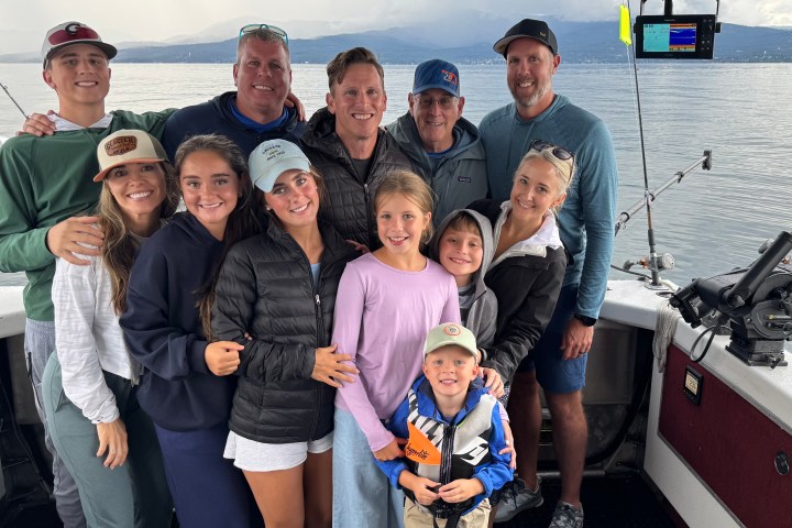 Group of people smiling on a boat with fishing rods and water in the background.