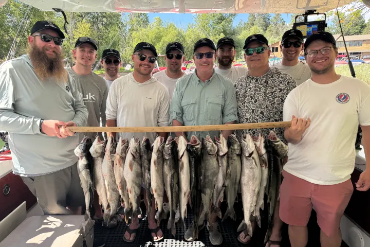 Group of men holding a wooden board displaying freshly caught fish on a boat.