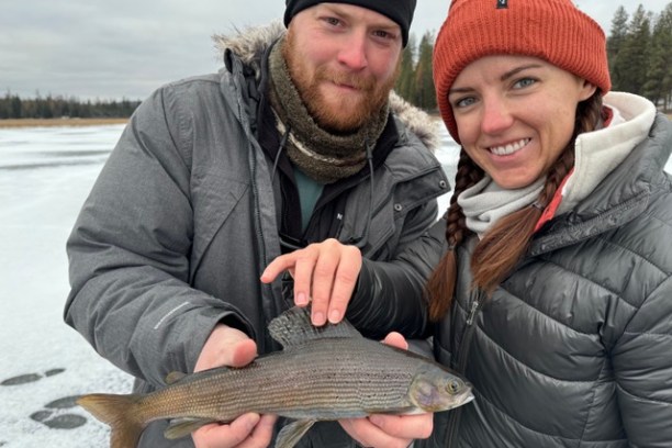 Two people holding a fish on an icy landscape.