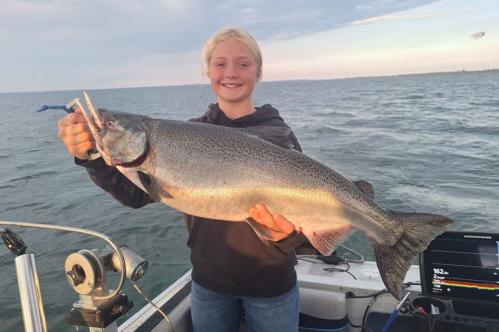 Person on a boat holding a large fish with ocean in the background.