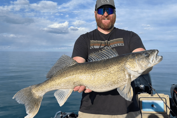 Man in cap holding large fish on a boat in a calm lake.