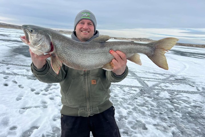 Person holding large fish on ice-covered lake with cloudy sky.