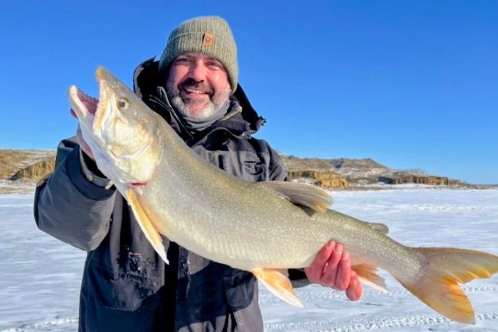 Person holding large fish on snowy landscape with blue sky.