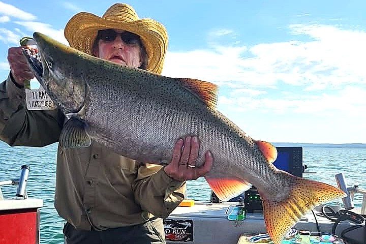 Person in a straw hat holding a large fish on a boat.