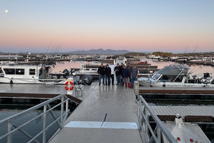 Group of people on a dock with boats and a sunset in the background.